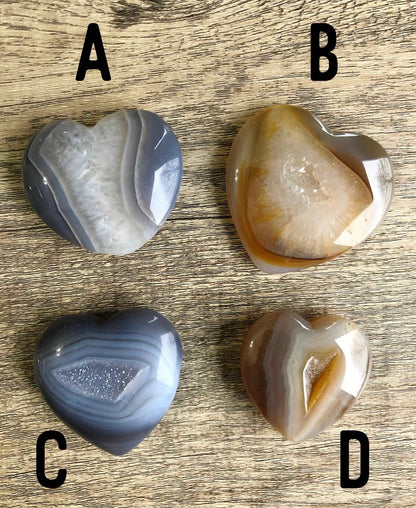 A picture of multiple natural agate carved into the shape of a heart. Each heart has druzy quartz crystals in the agate.