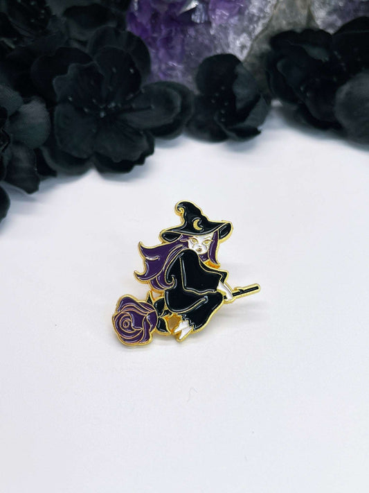 Pictured is an enamel pin of a witch flying on a broom that looks like a rose.