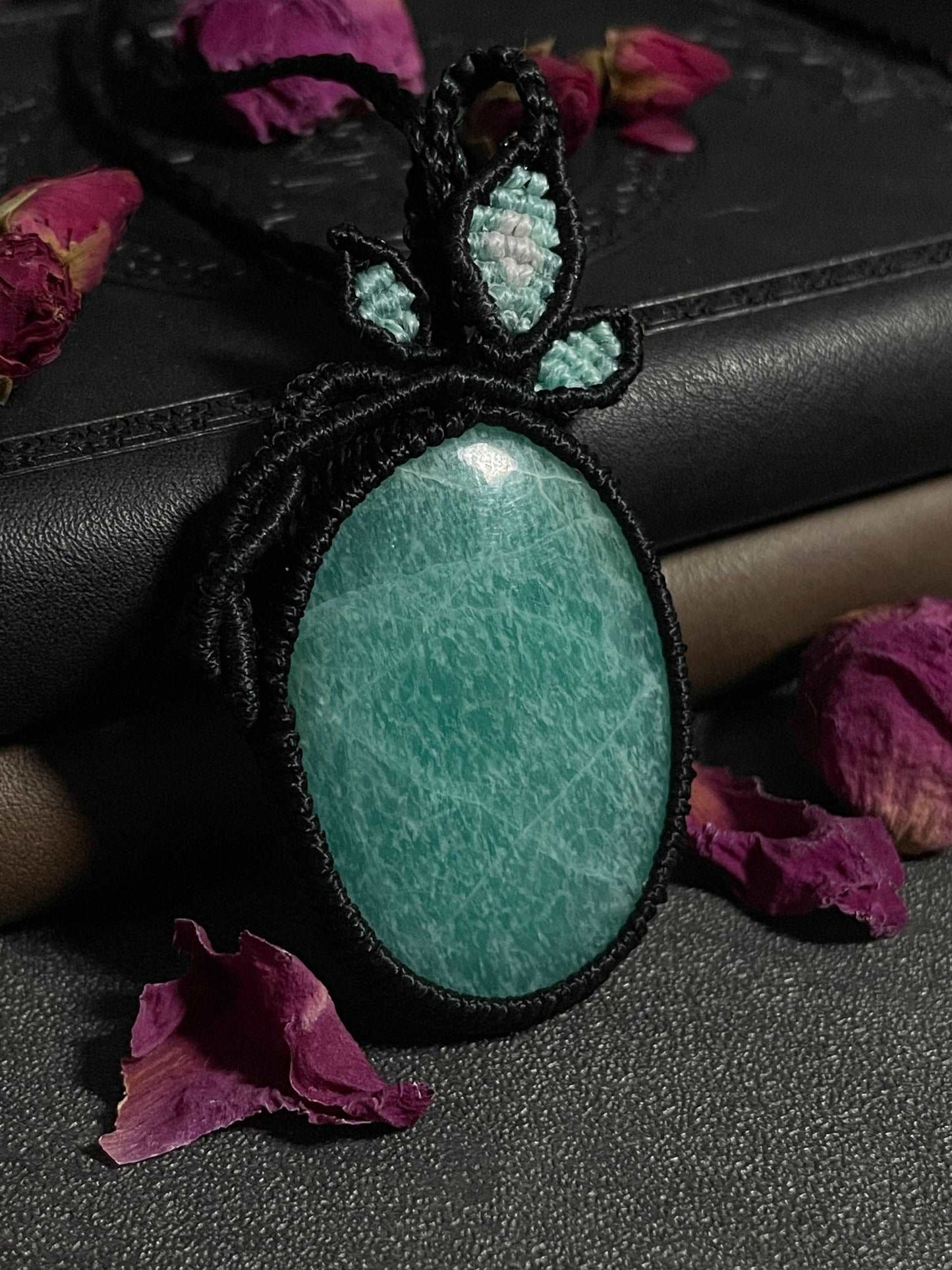 Pictured is an amazonite cabochon wrapped in macrame thread. A gothic book and flowers are nearby.