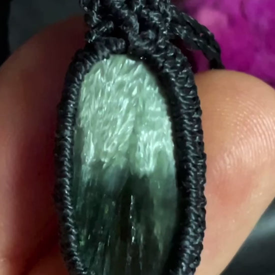 Pictured is a seraphinite cabochon wrapped in macrame thread. A gothic book and flowers are nearby.