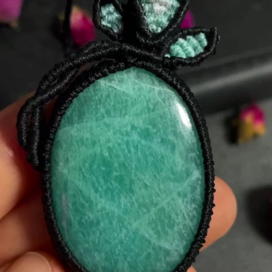 Pictured is an amazonite cabochon wrapped in macrame thread. A gothic book and flowers are nearby.