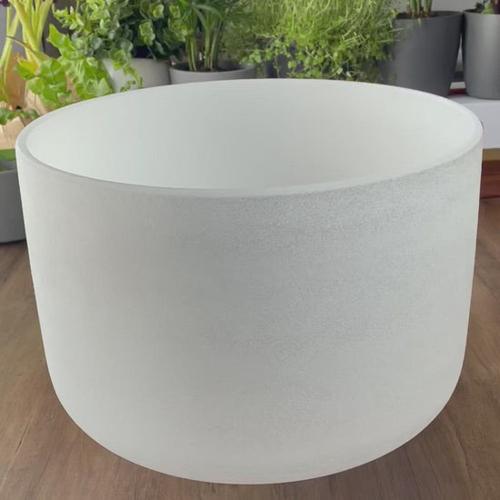  A photo of a quartz crystal singing bowl and a mallet on a wooden surface. The crystal singing bowl is made of clear quartz and has a smooth, round shape.