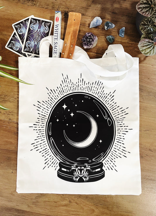 Pictured is a large canvas tote bag featuring an image of a crystal ball with a crescent moon inside.