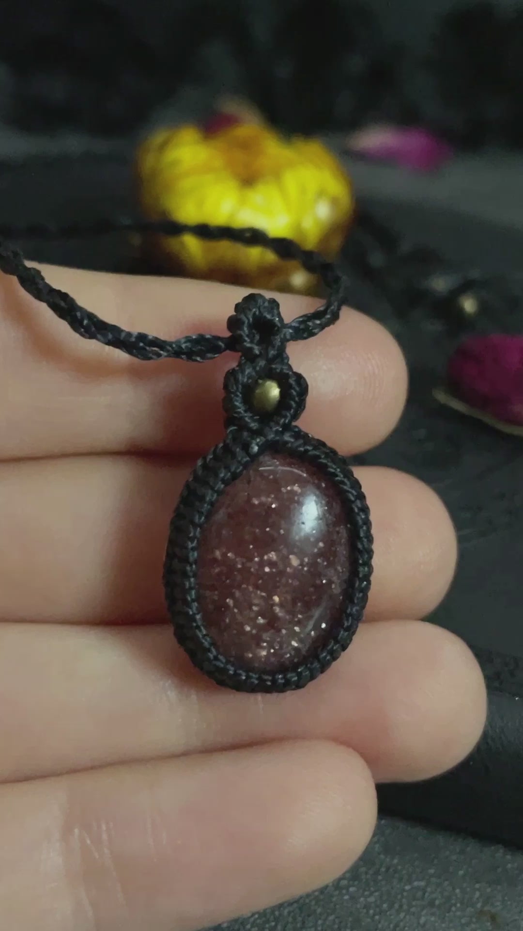 Pictured is a strawberry quartz cabochon wrapped in macrame thread. A gothic book and flowers are nearby.