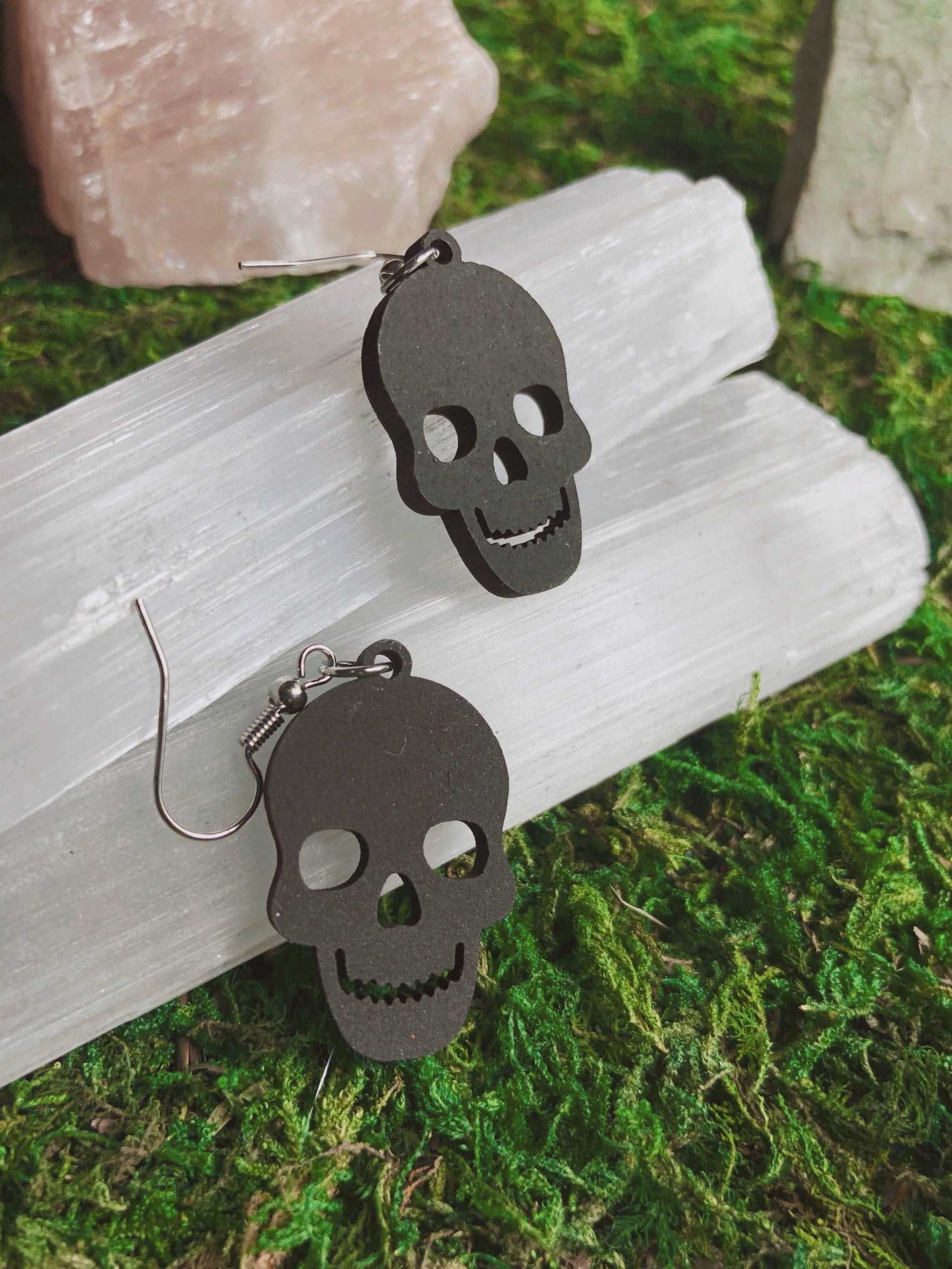 Pictured is a pair of black earrings featuring a skull. They are made of wood. 