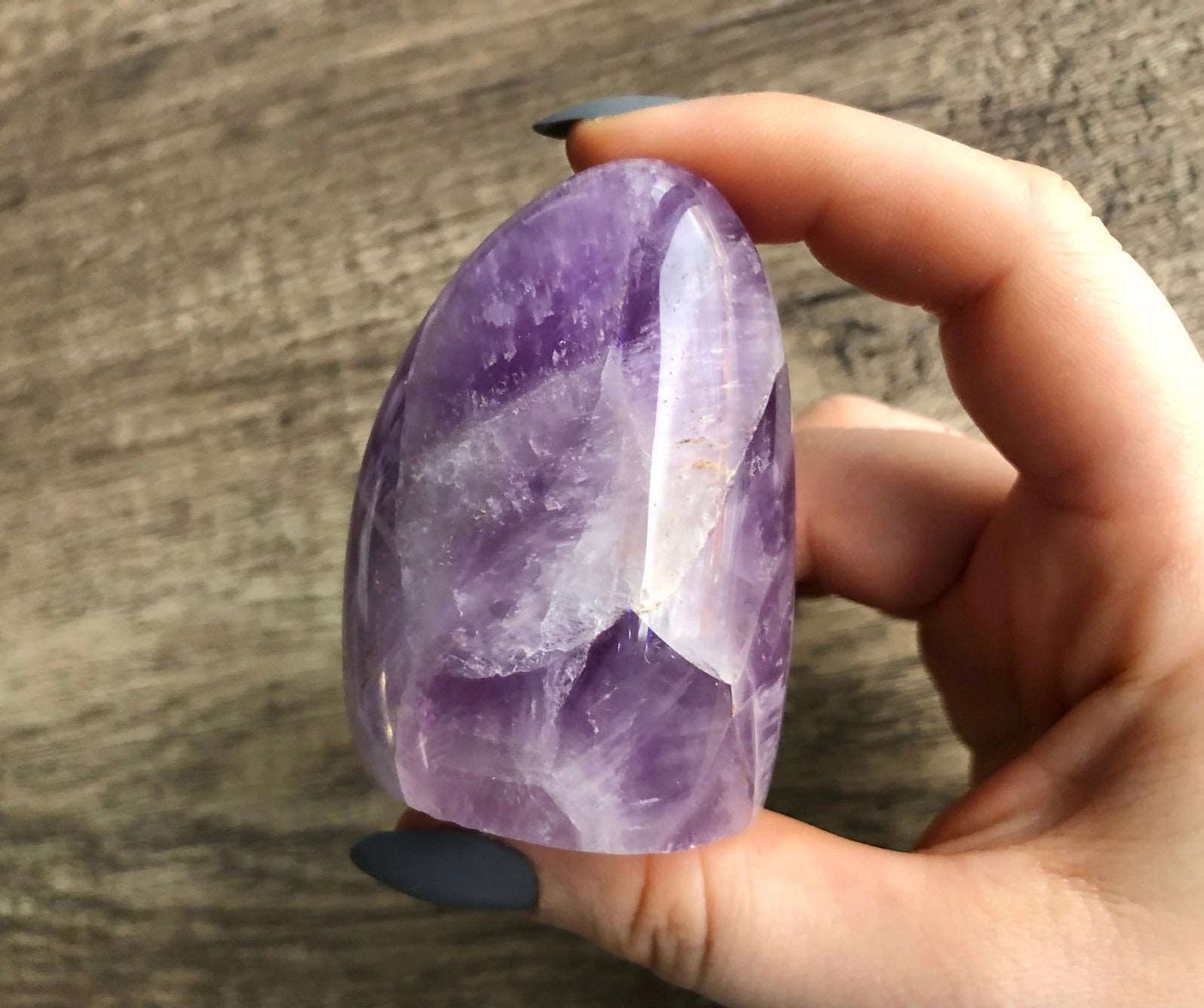 A small freestanding polished piece of amethyst is shown in the image. The crystal is a deep purple color and has a smooth, shiny surface.