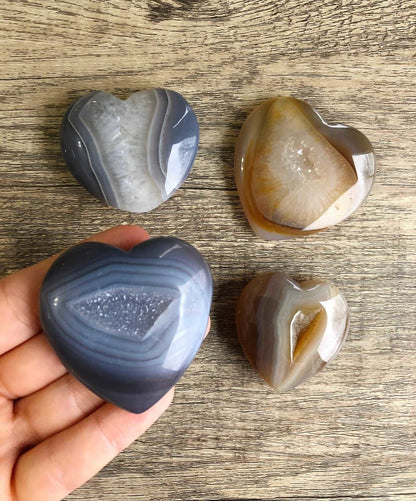 A picture of multiple natural agate carved into the shape of a heart. Each heart has druzy quartz crystals in the agate.
