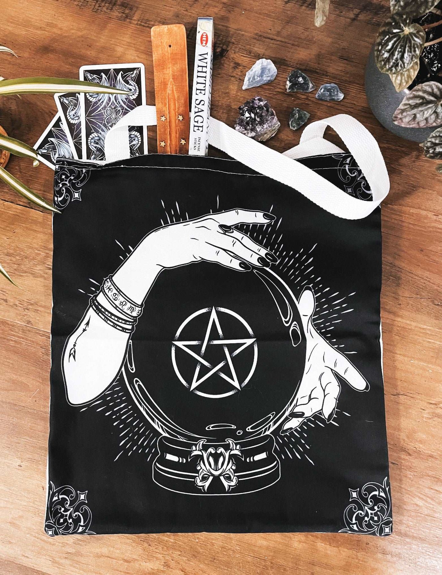 Pictured is a large canvas tote bag featuring an image of a black crystal ball with hands around it and a pentagram in the middle of the crystal ball.