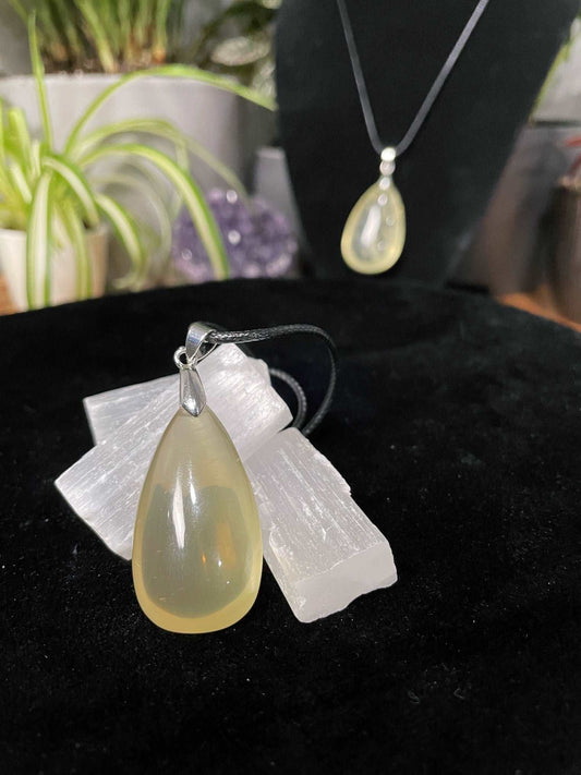 An image of a citrine teardrop shaped pendant on a necklace. It sits atop some selenite chunks and a black velvet surface.