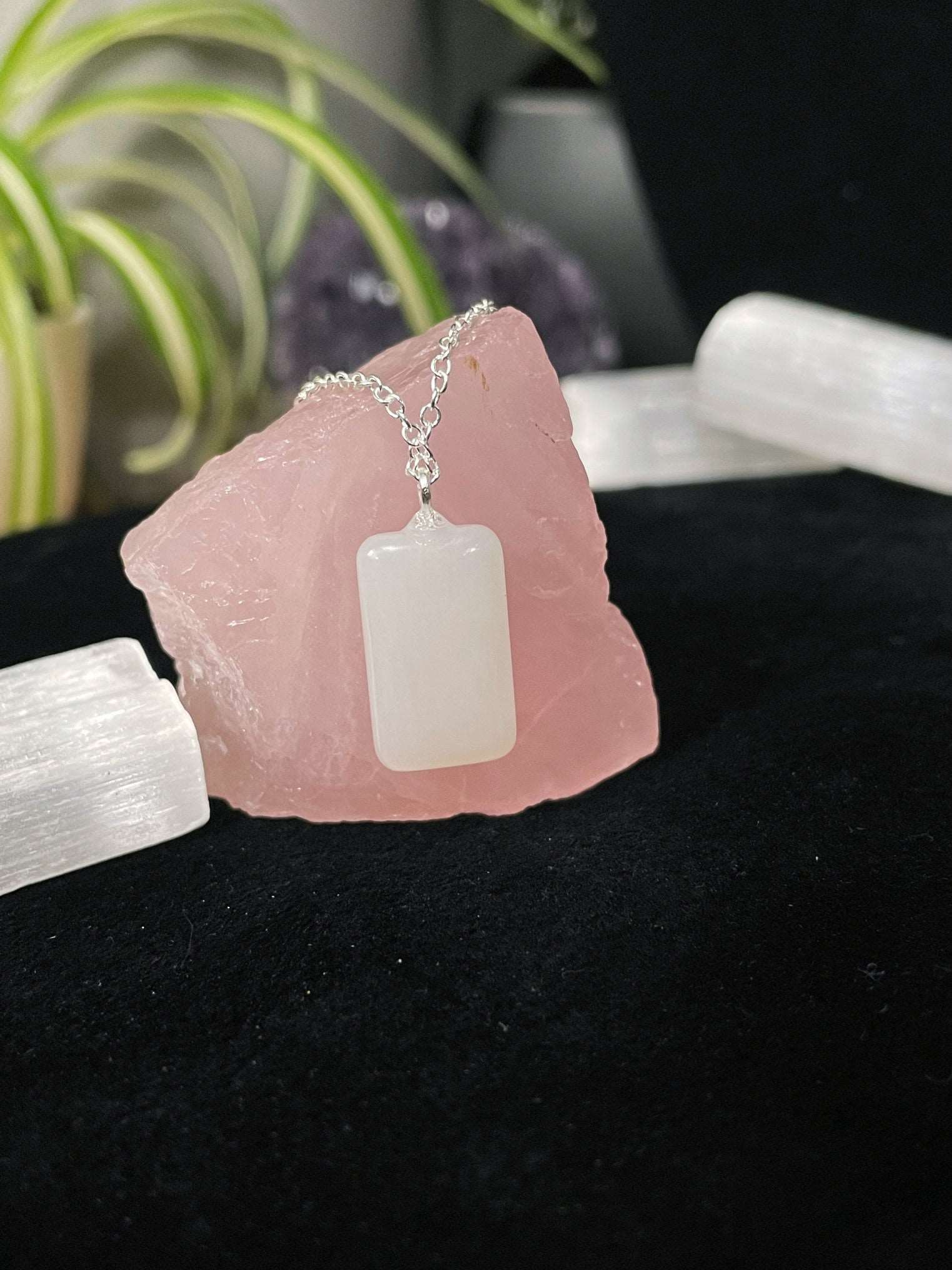 An image of a genuine hetian white jade rectangle shaped pendant on a necklace. It sits atop some selenite chunks and a black velvet surface.