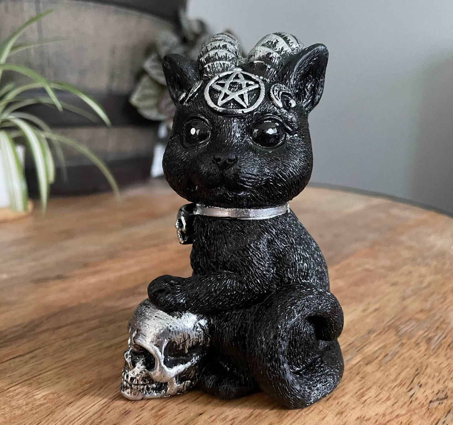 Pictured is a resin statue of a black cat with horns and a pentagram on its forehead with a paw on a silver skull.