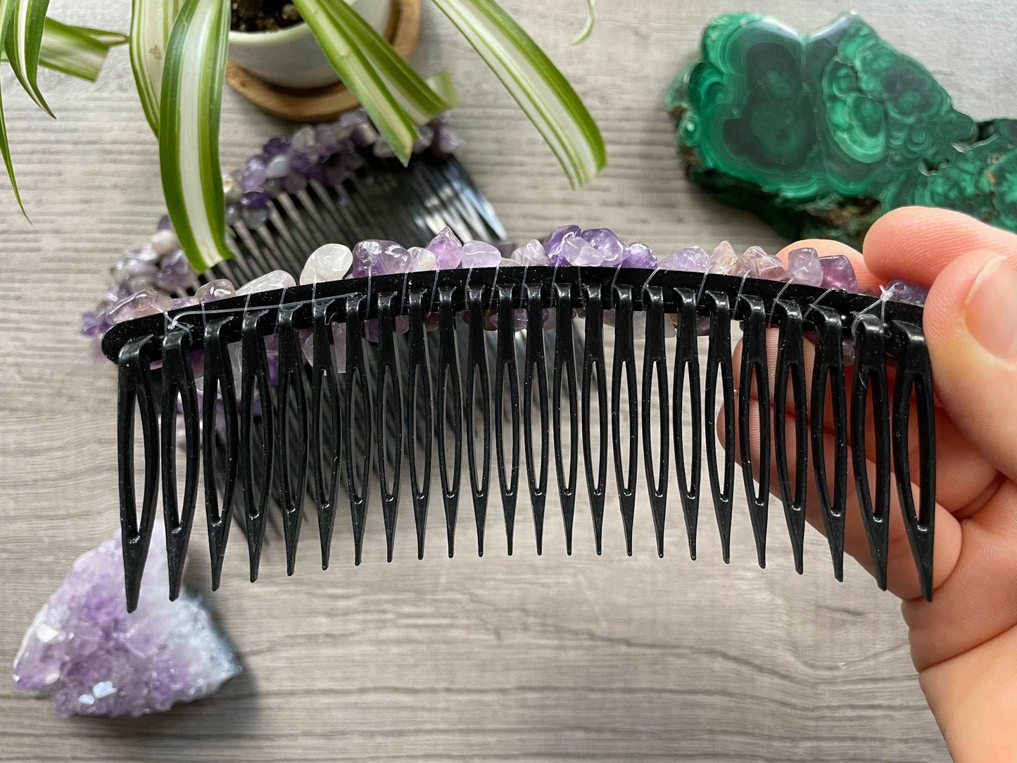 An image of several black hair combs with tumbled amethyst crystals across the top. A slab of malachite and an amethyst cluster sits nearby.