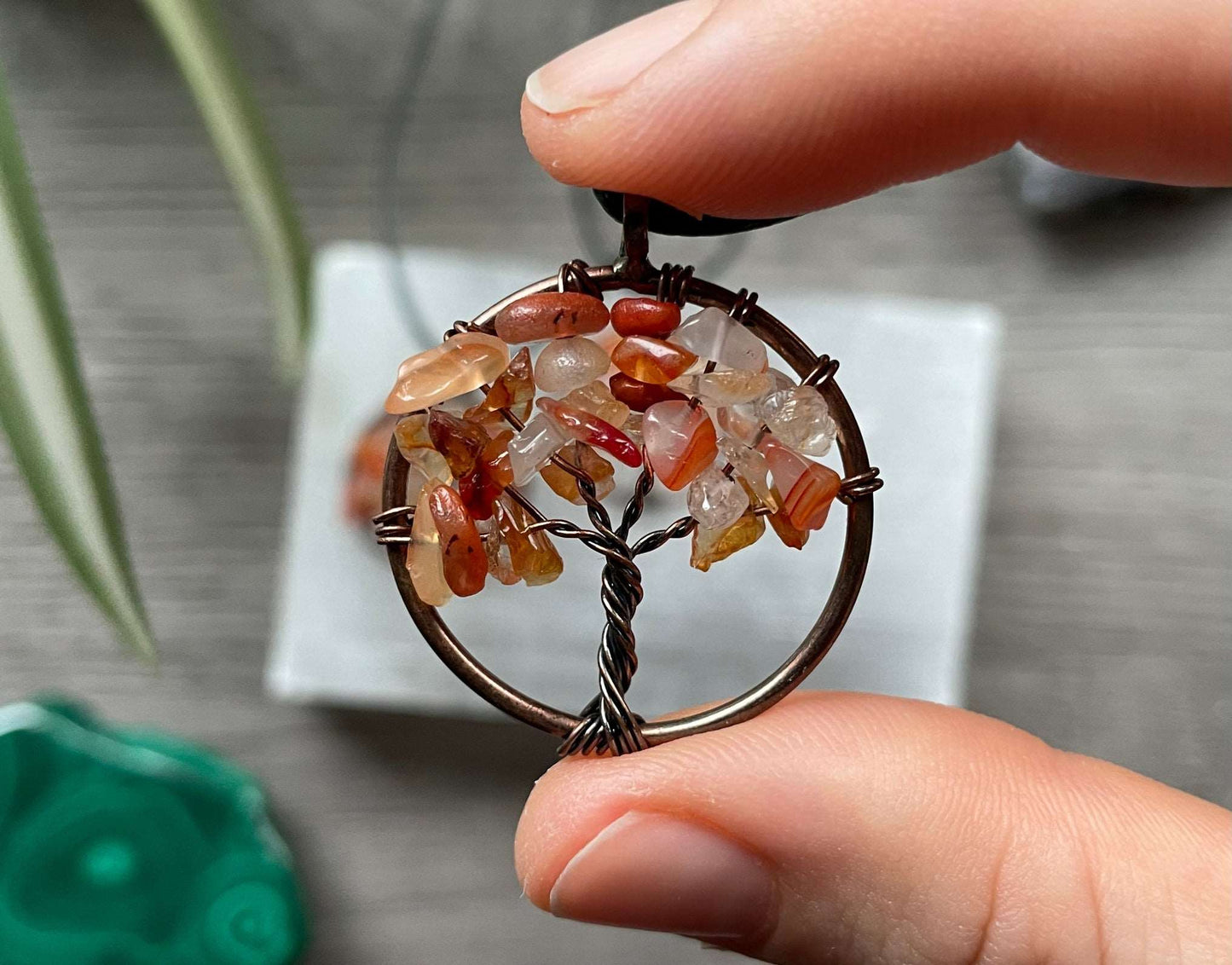 An image of a necklace featuring a wire-wrapped pendant. The wire is in the shape of a tree and the leaves on the tree are polished chips of carnelian.