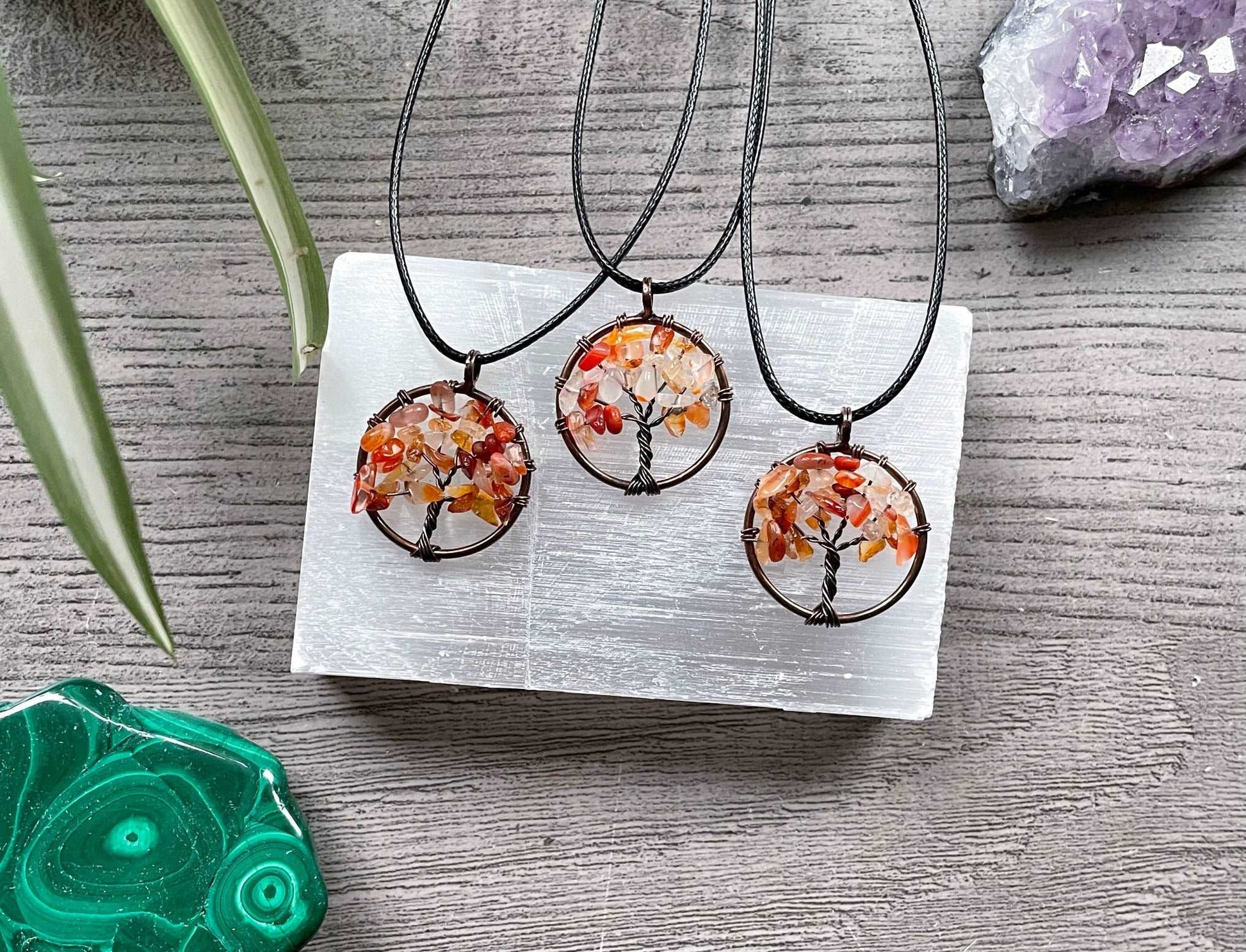 An image of a necklace featuring a wire-wrapped pendant. The wire is in the shape of a tree and the leaves on the tree are polished chips of carnelian.