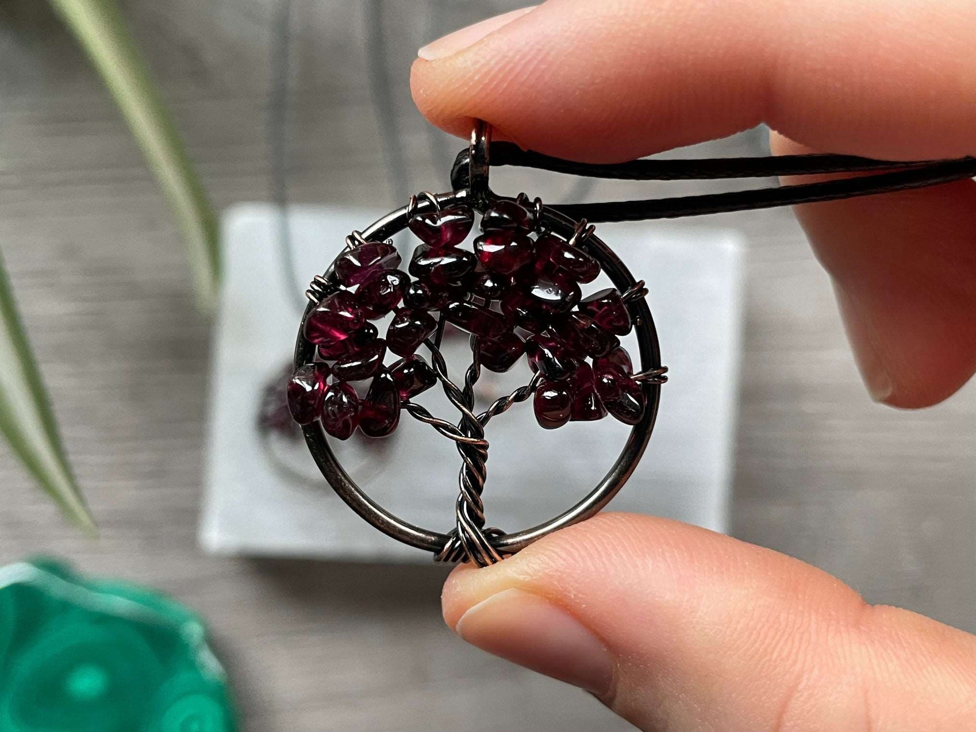 An image of a necklace featuring a wire-wrapped pendant. The wire is in the shape of a tree and the leaves on the tree are polished chips of garnet.