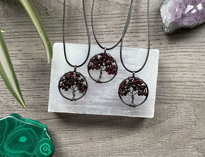 An image of a necklace featuring a wire-wrapped pendant. The wire is in the shape of a tree and the leaves on the tree are polished chips of garnet.