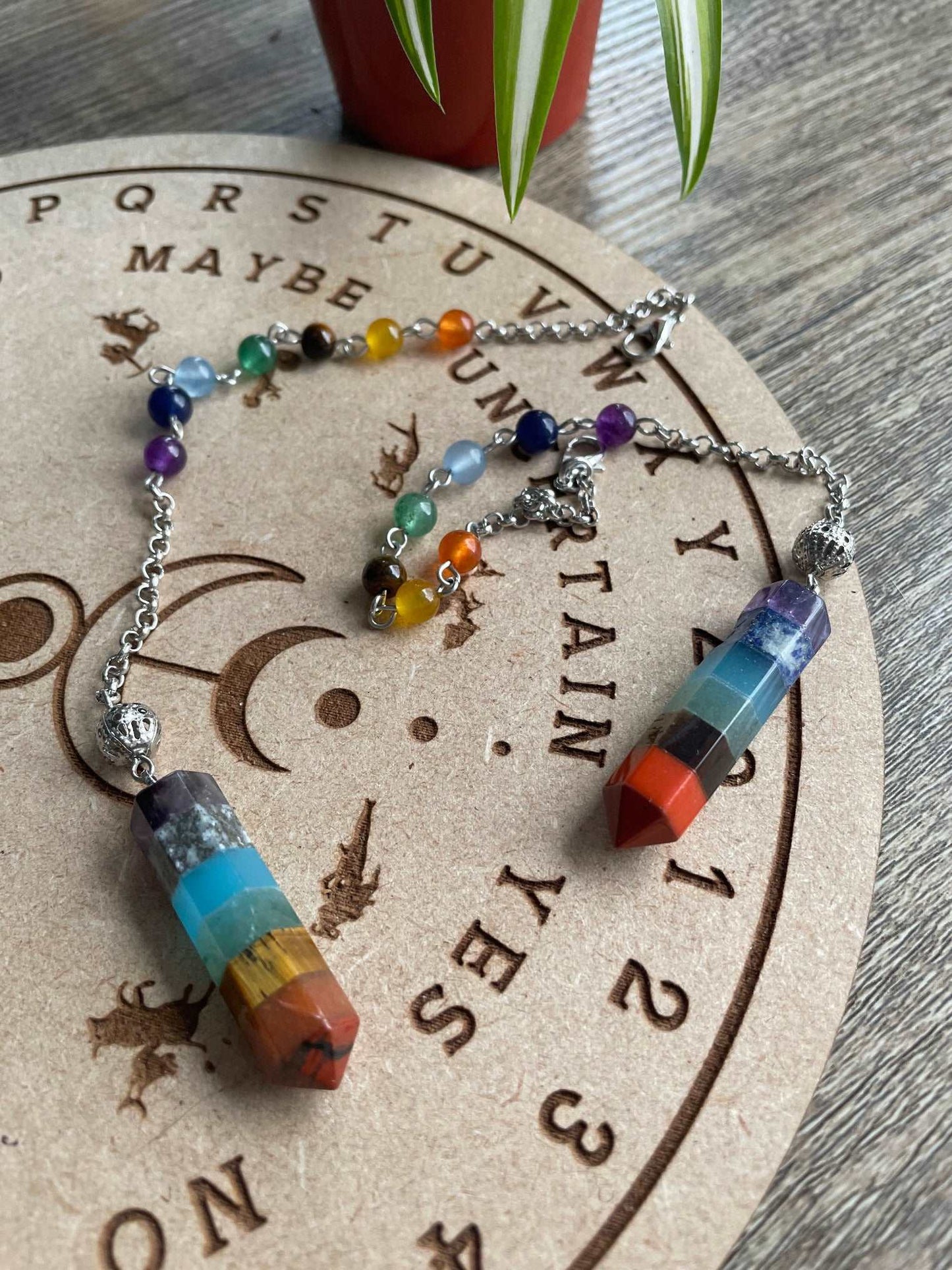A multicoloured crystal pendulum sits atop a wooden divination board.
