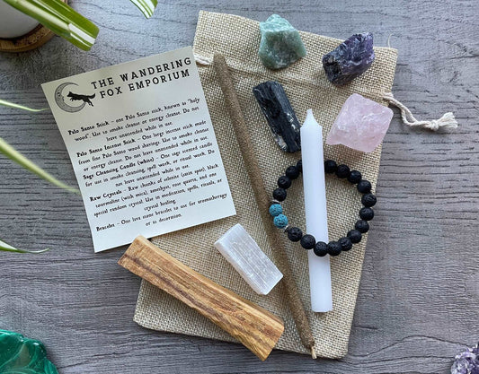 Pictured is a crystal starter set with various raw crystals, incense, a bracelet, a candle, and a palo santo stick. A piece of paper is nearby with the information about the crystals on it.