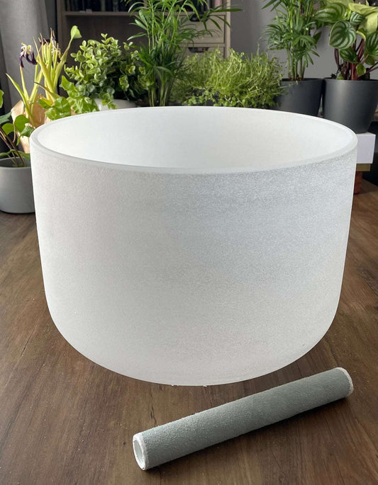  A photo of a quartz crystal singing bowl and a mallet on a wooden surface. The crystal singing bowl is made of clear quartz and has a smooth, round shape.