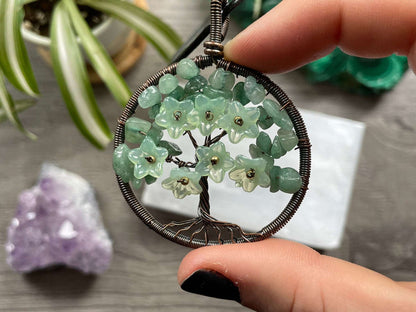 An image of a necklace featuring a wire-wrapped pendant. The wire is in the shape of a tree and the leaves on the tree are polished chips of green aventurine.