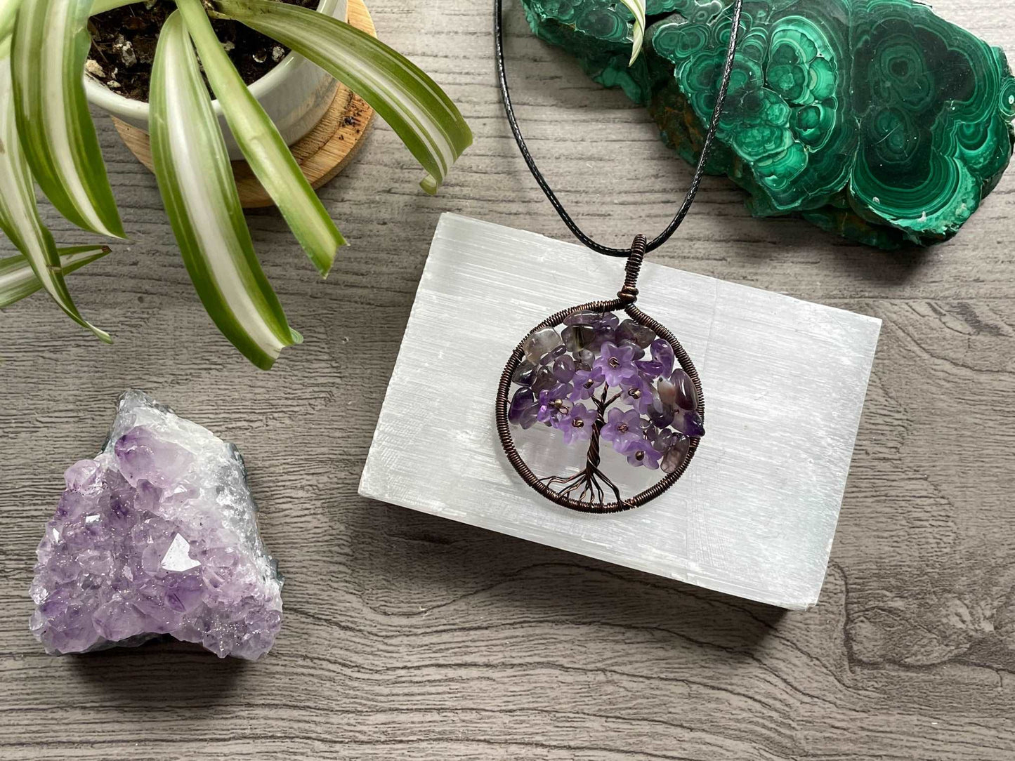 An image of a necklace featuring a wire-wrapped pendant. The wire is in the shape of a tree and the leaves on the tree are polished chips of amethyst.