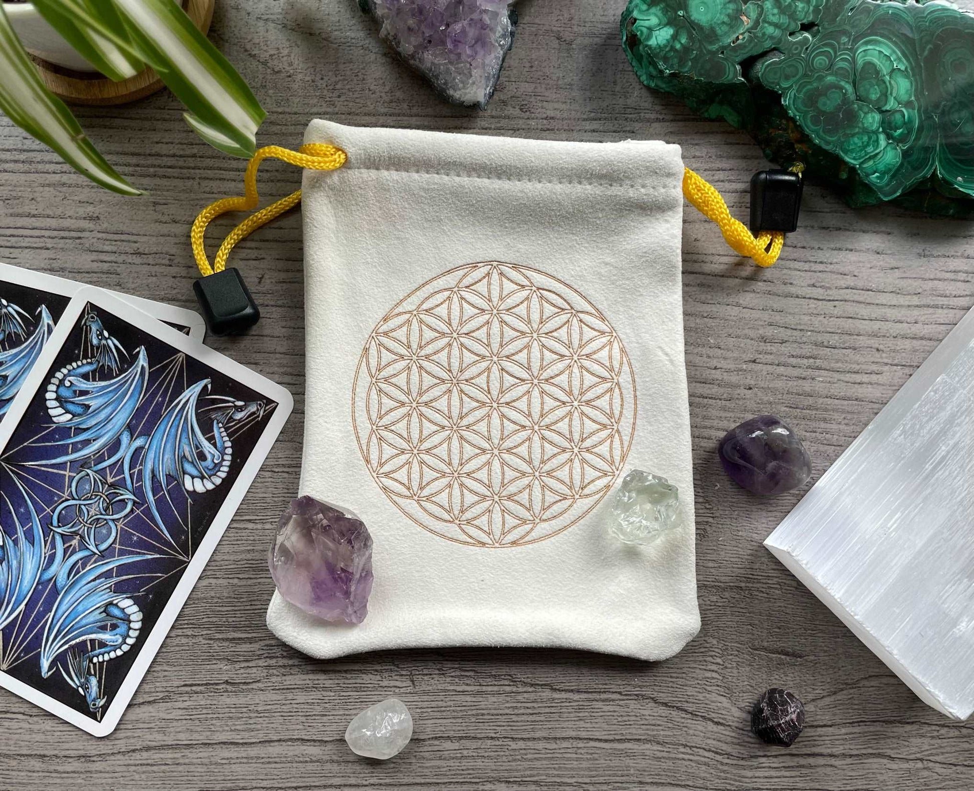 Pictured is a cream-coloured, faux-suede drawstring bag with a flower of life printed on the front.