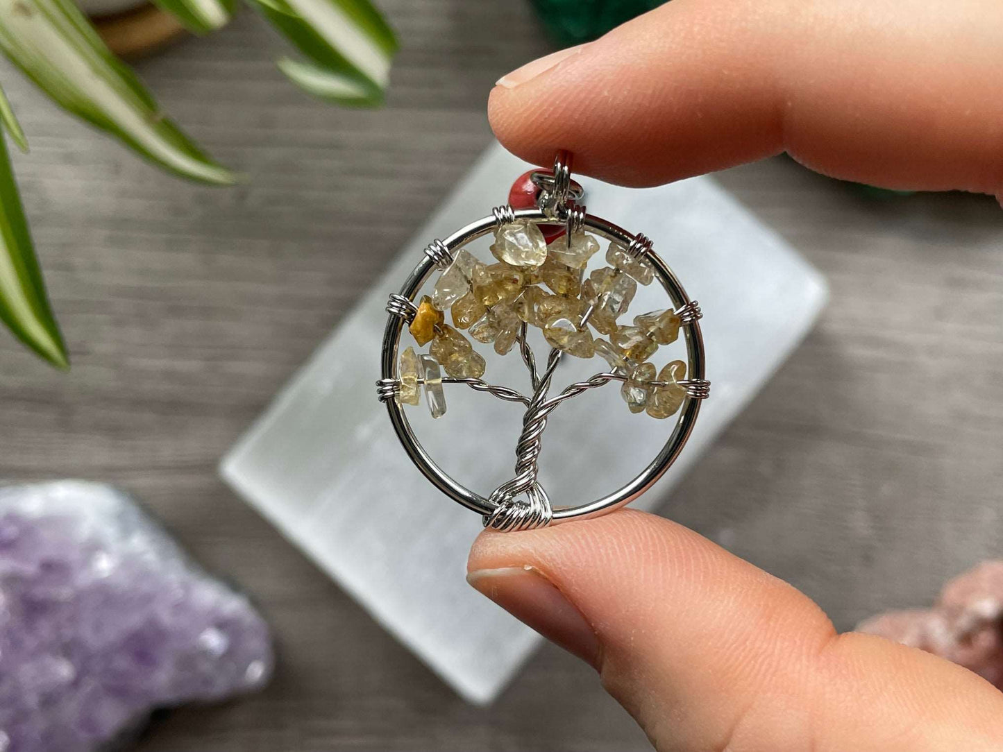 A tree of life with citrine crystals as the leaves on the tree is in the image. The keychain has a number of small multi-coloured beads to represent the chakras on the chain. The keychain sits atop a slab of selenite. Malachite, pink amethyst, and amethyst are nearby.