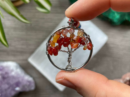 A tree of life with carnelian crystals as the leaves on the tree is in the image. The keychain has a number of small multi-coloured beads to represent the chakras on the chain. The keychain sits atop a slab of selenite. Malachite, pink amethyst, and amethyst are nearby.