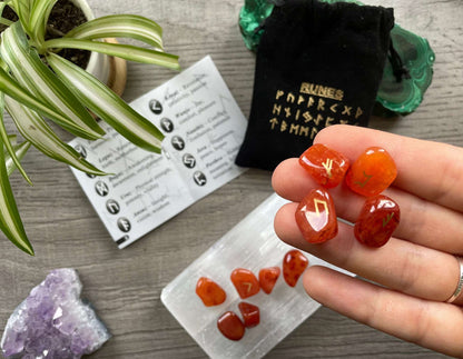 Pictured is a rune set made of carnelian tumbled stones. A black velvet bag and instructions sit nearby,