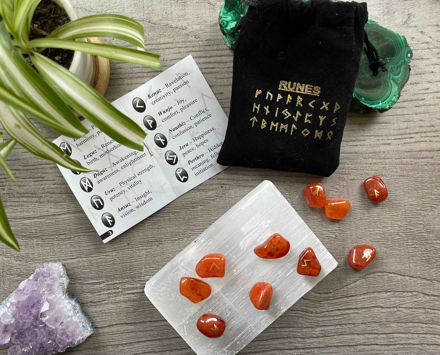 Pictured is a rune set made of carnelian tumbled stones. A black velvet bag and instructions sit nearby,