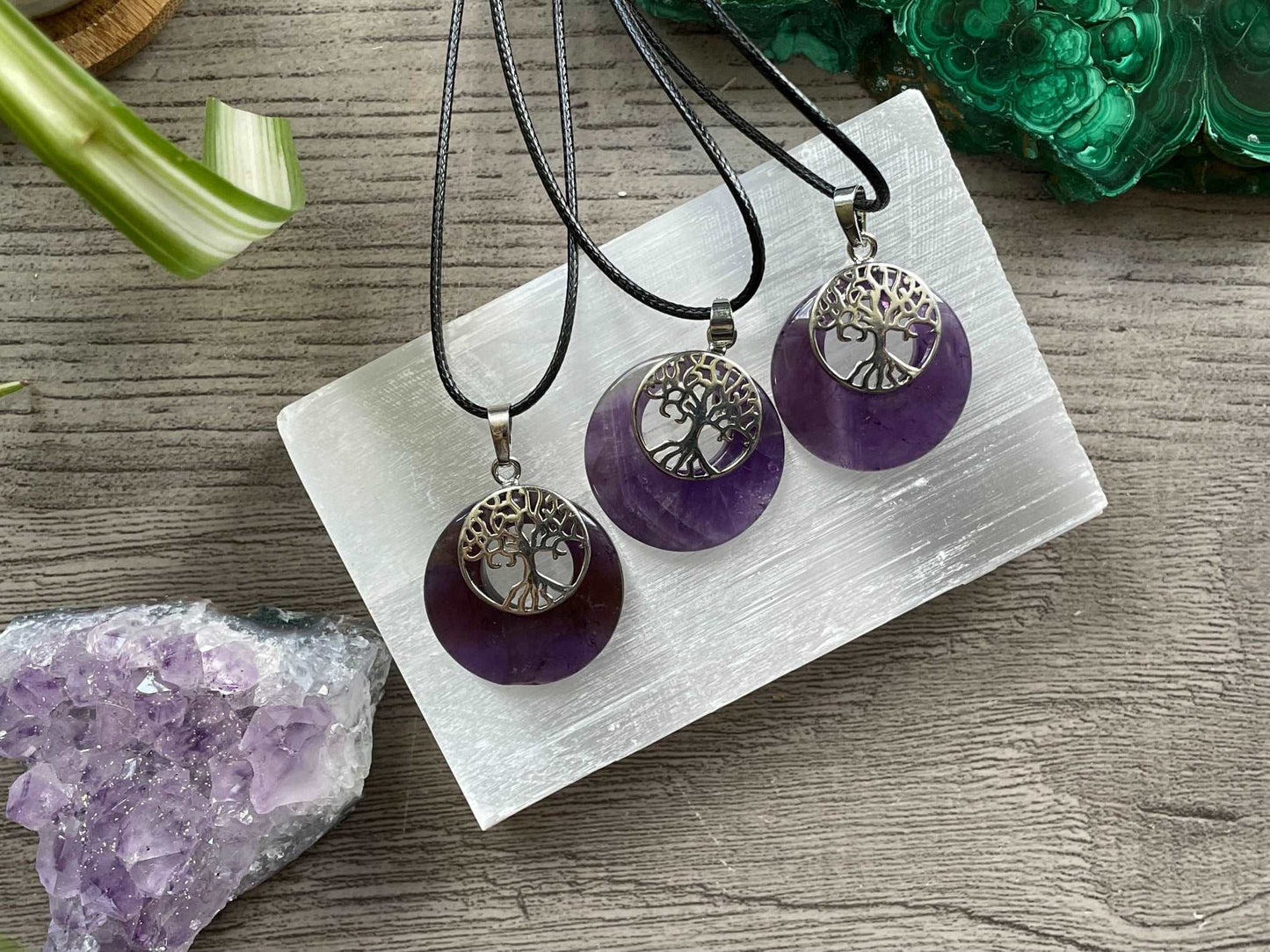 An image of a circular amethyst necklace with a silver coloured tree of life charm over top of the amethyst.