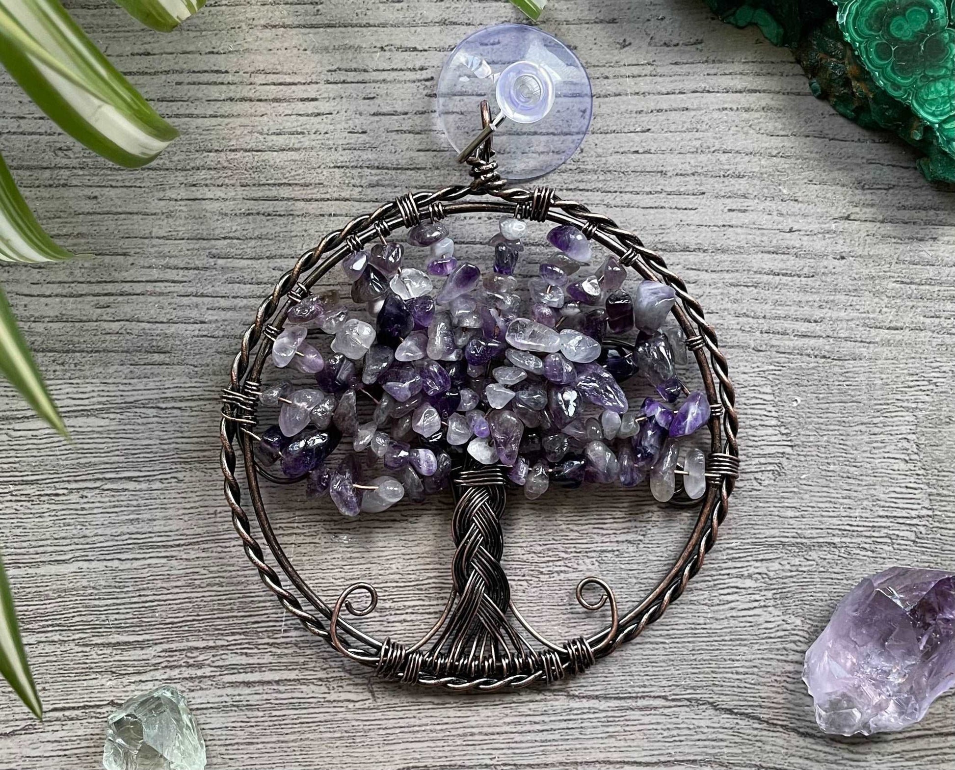 An image of a window art piece with a suction cup. The art is a wire-wrapped tree of life and the leaves on the tree are polished chips of amethyst.