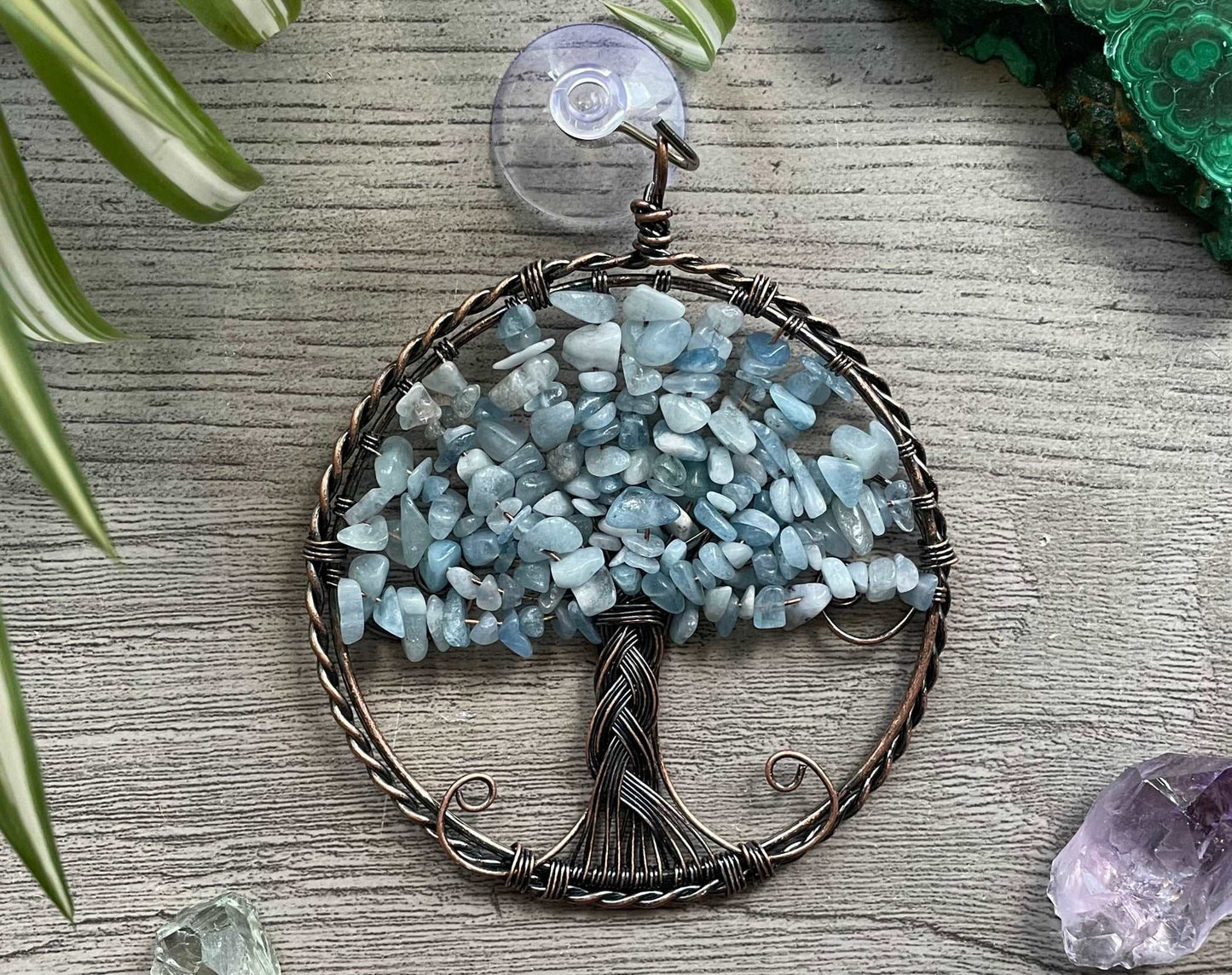 An image of a window art piece with a suction cup. The art is a wire-wrapped tree of life and the leaves on the tree are polished chips of aquamarine.