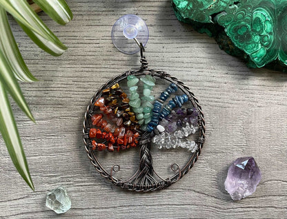 An image of a window art piece with a suction cup. The art is a wire-wrapped tree of life and the leaves on the tree are polished chips of green aventurine, red jasper, carnelian, tiger's eye, aquamarine, amethyst, and clear quartz.