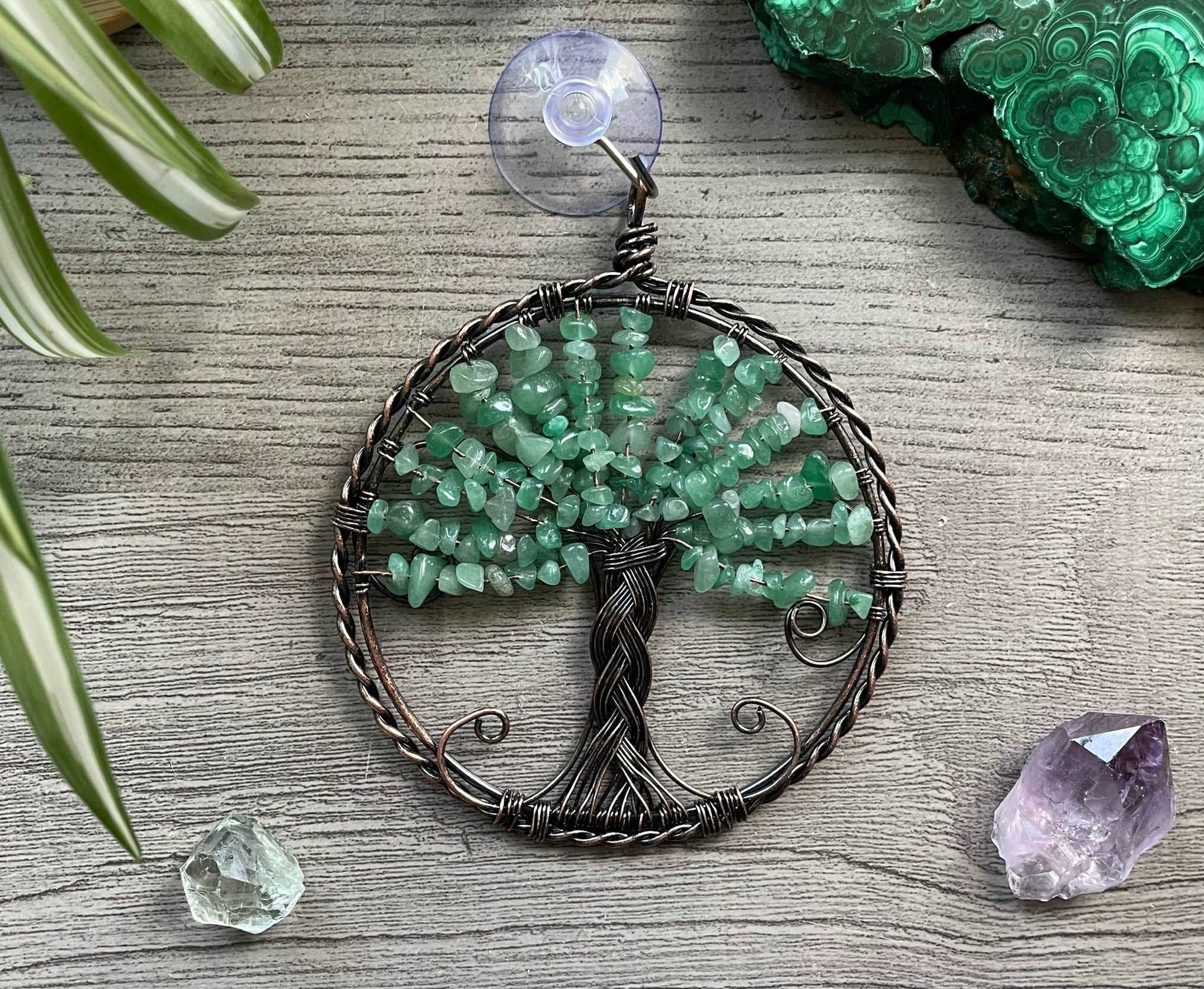 An image of a window art piece with a suction cup. The art is a wire-wrapped tree of life and the leaves on the tree are polished chips of green aventurine.