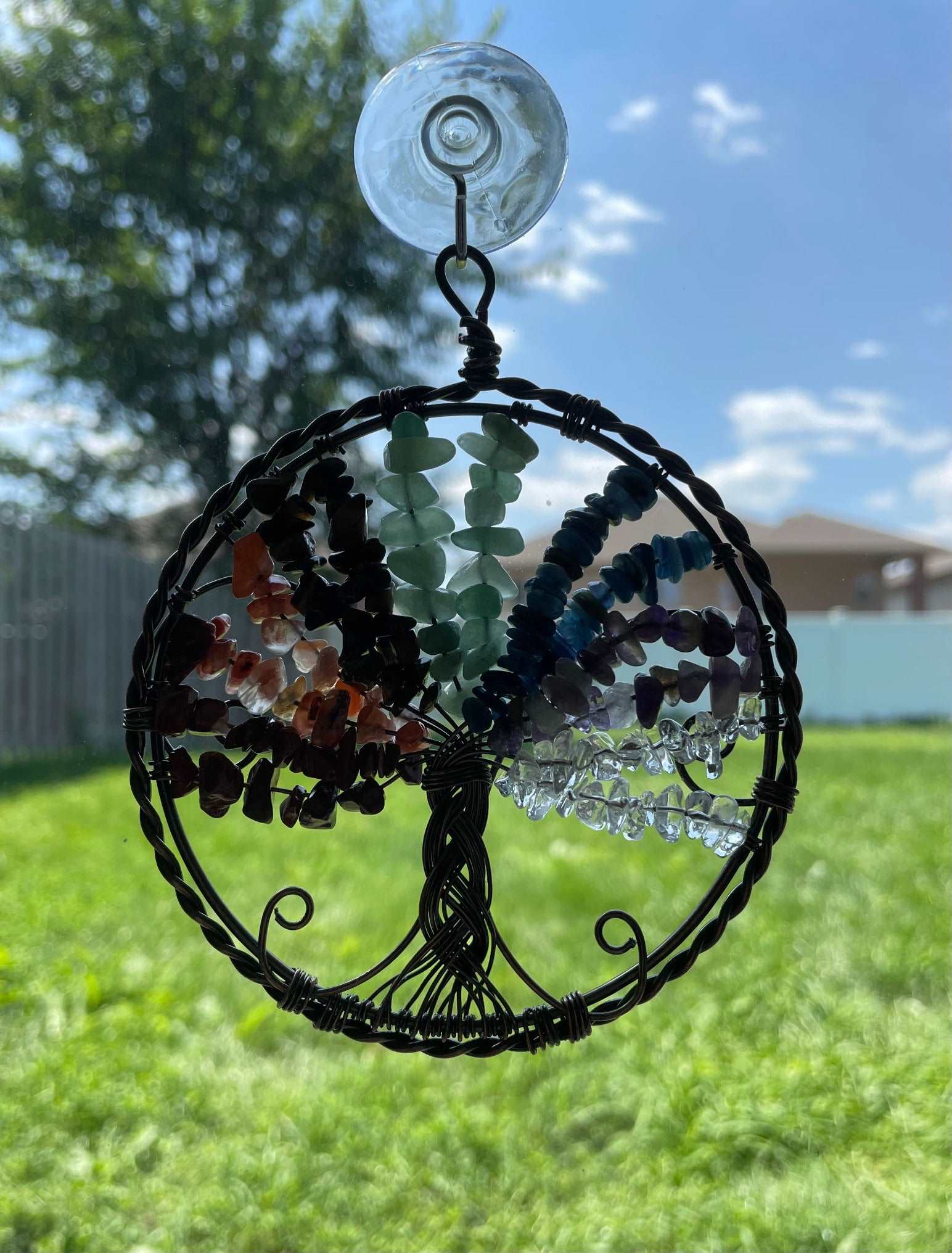 An image of a window art piece with a suction cup. The art is a wire-wrapped tree of life and the leaves on the tree are polished chips of green aventurine, red jasper, carnelian, tiger's eye, aquamarine, amethyst, and clear quartz.