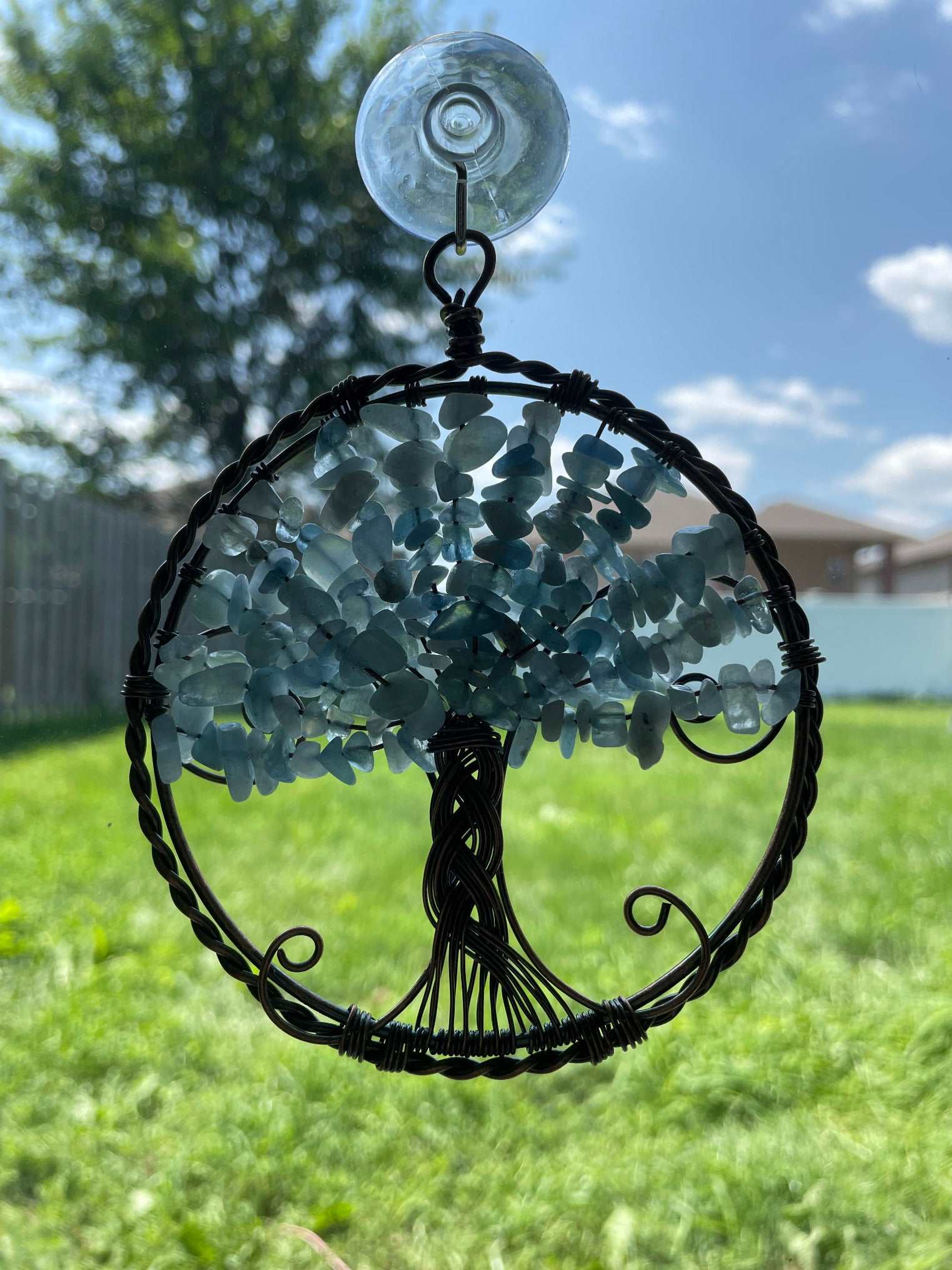 An image of a window art piece with a suction cup. The art is a wire-wrapped tree of life and the leaves on the tree are polished chips of aquamarine.