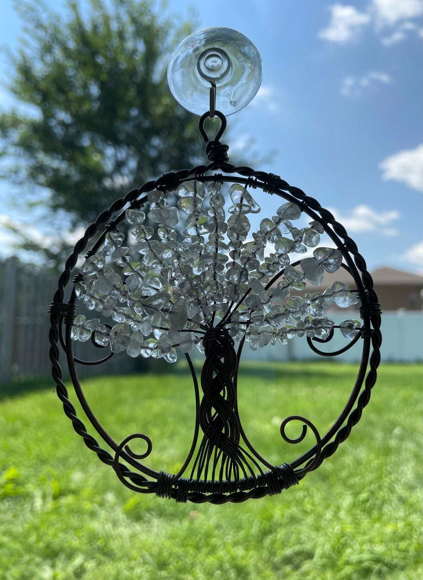 An image of a window art piece with a suction cup. The art is a wire-wrapped tree of life and the leaves on the tree are polished chips of clear quartz.