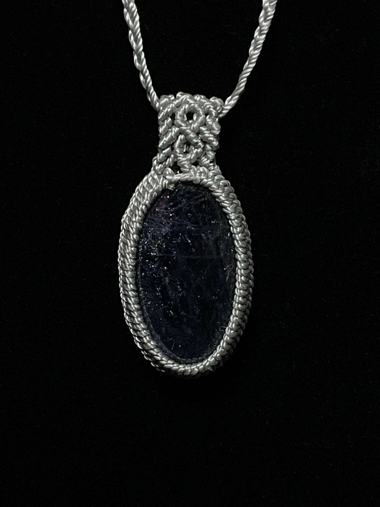 Pictured is an iolite cabochon wrapped in macrame thread. A gothic book and flowers are nearby.