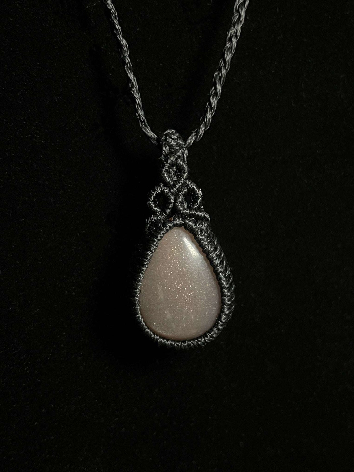 Pictured is a grey moonstone cabochon wrapped in macrame thread. A gothic book and flowers are nearby.