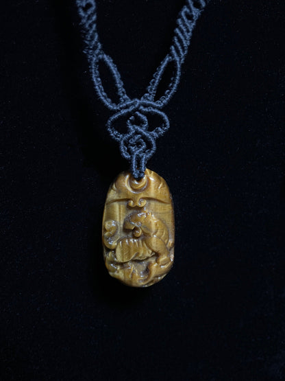 A picture of a tiger pendant carved out of tiger's eye stone. The pendant is on an intricate black macrame necklace.