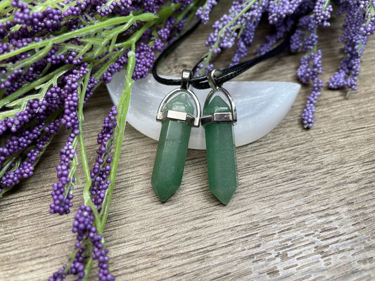 An image of green aventurine double-terminated polished crystal necklaces sitting on selenite and surrounded by lavender on a wood surface..