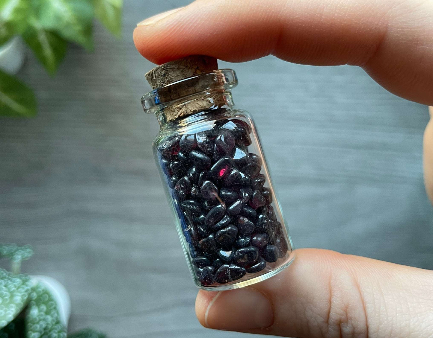 Pictured is a small glass vial with a cork stopper. Inside the jar are garnet chips.