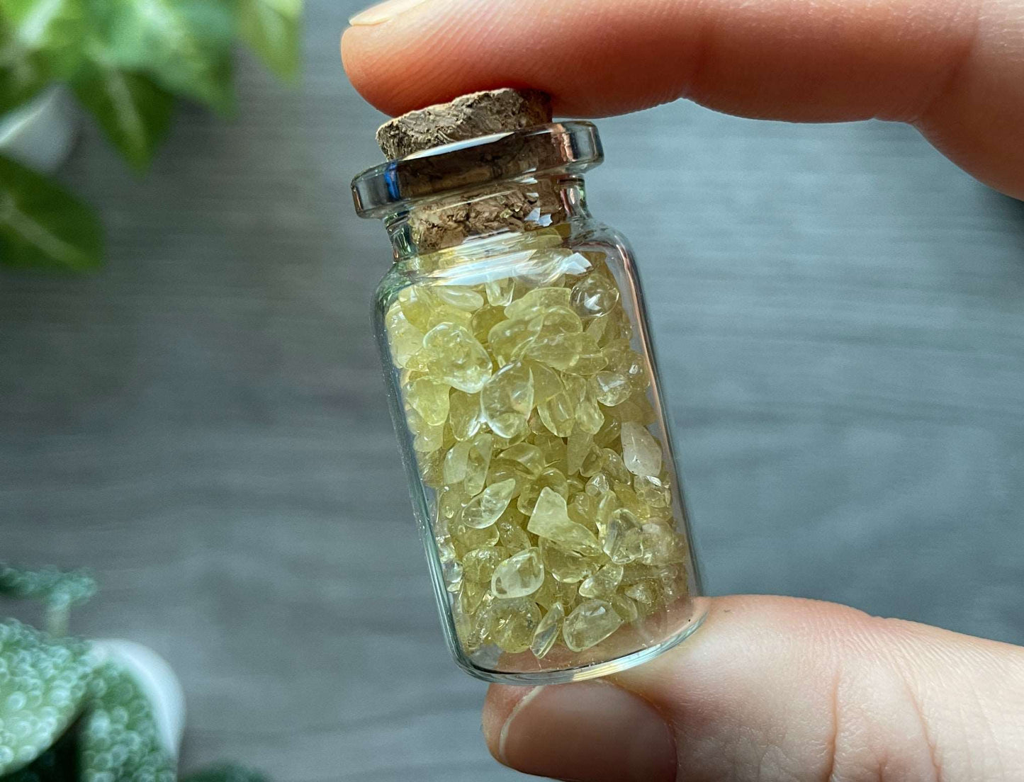 Pictured is a small glass vial with a cork stopper. Inside the jar are citrine chips.