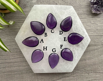An image of high-quality purple amethyst cabochons. The cabochons are teardrop shaped and arranged in the shape of a flower.