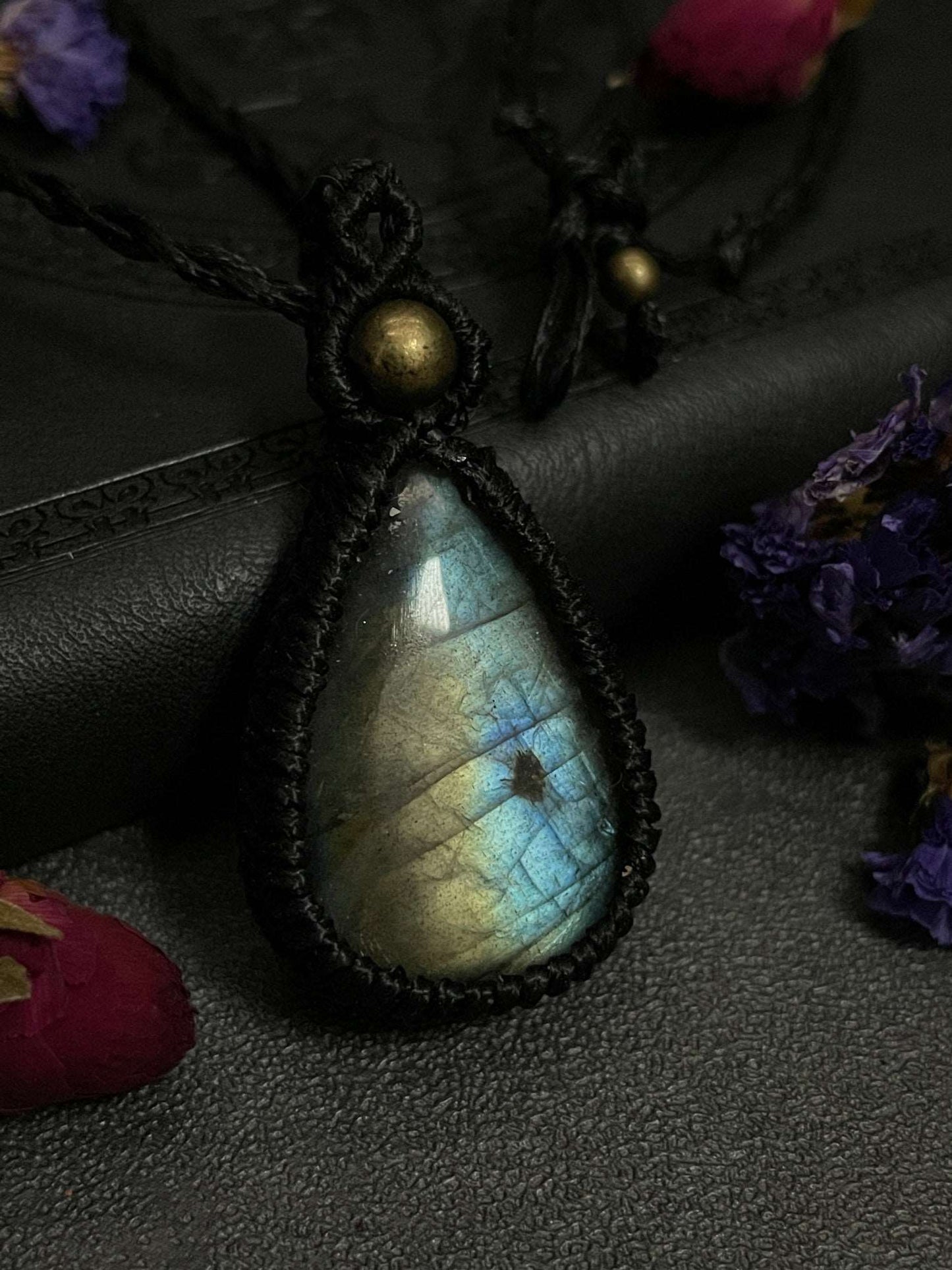 Pictured is a labradorite cabochon wrapped in macrame thread. A gothic book and flowers are nearby.