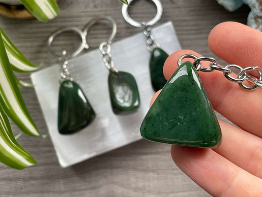 A keychain with a tumbled piece of genuine Canadian jade (nephrite jade) on it. The keychain sits atop a slab of selenite.