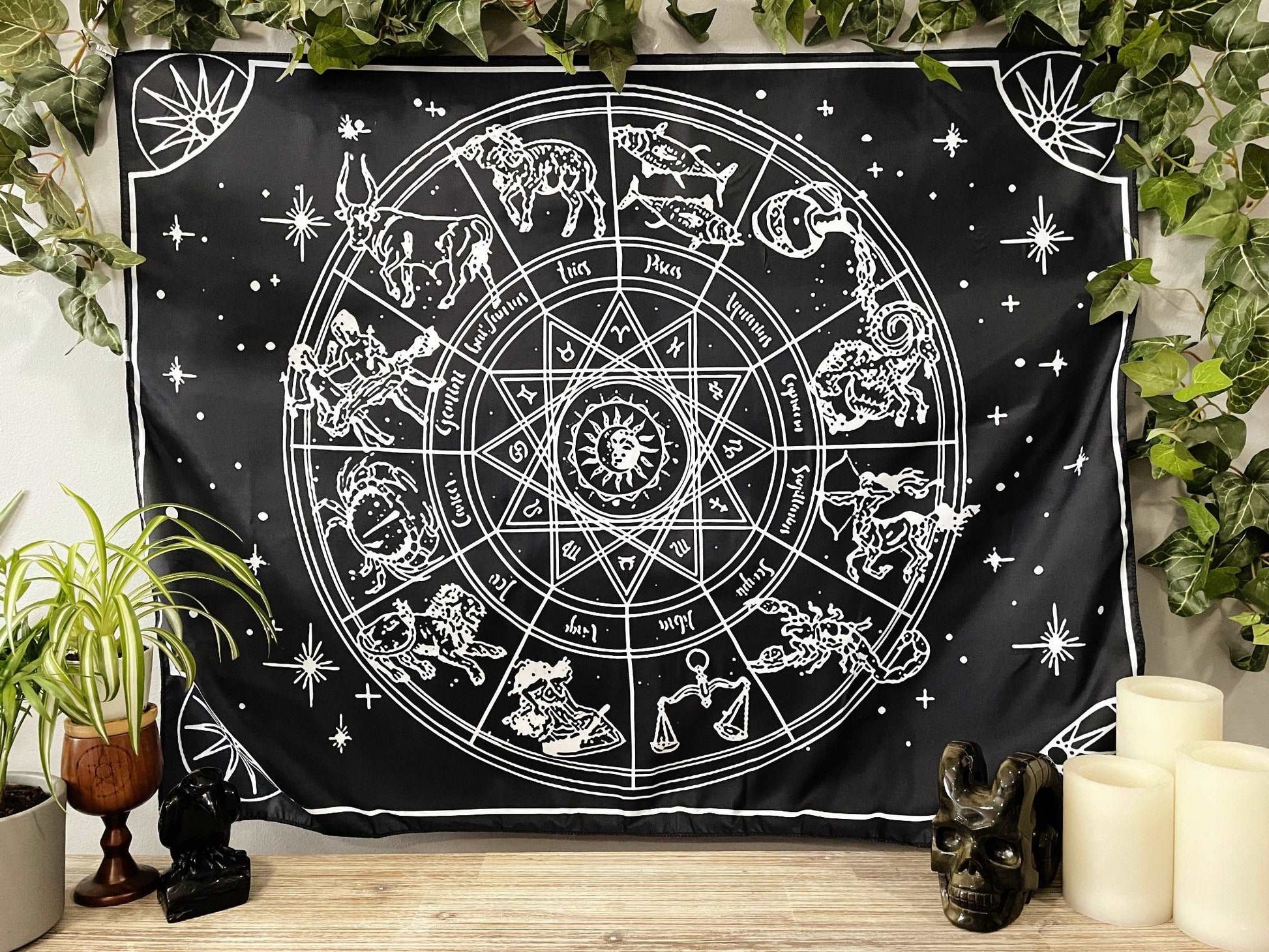 Pictured is a large wall tapestry with a black background and a large zodiac wheel printed in white on it.