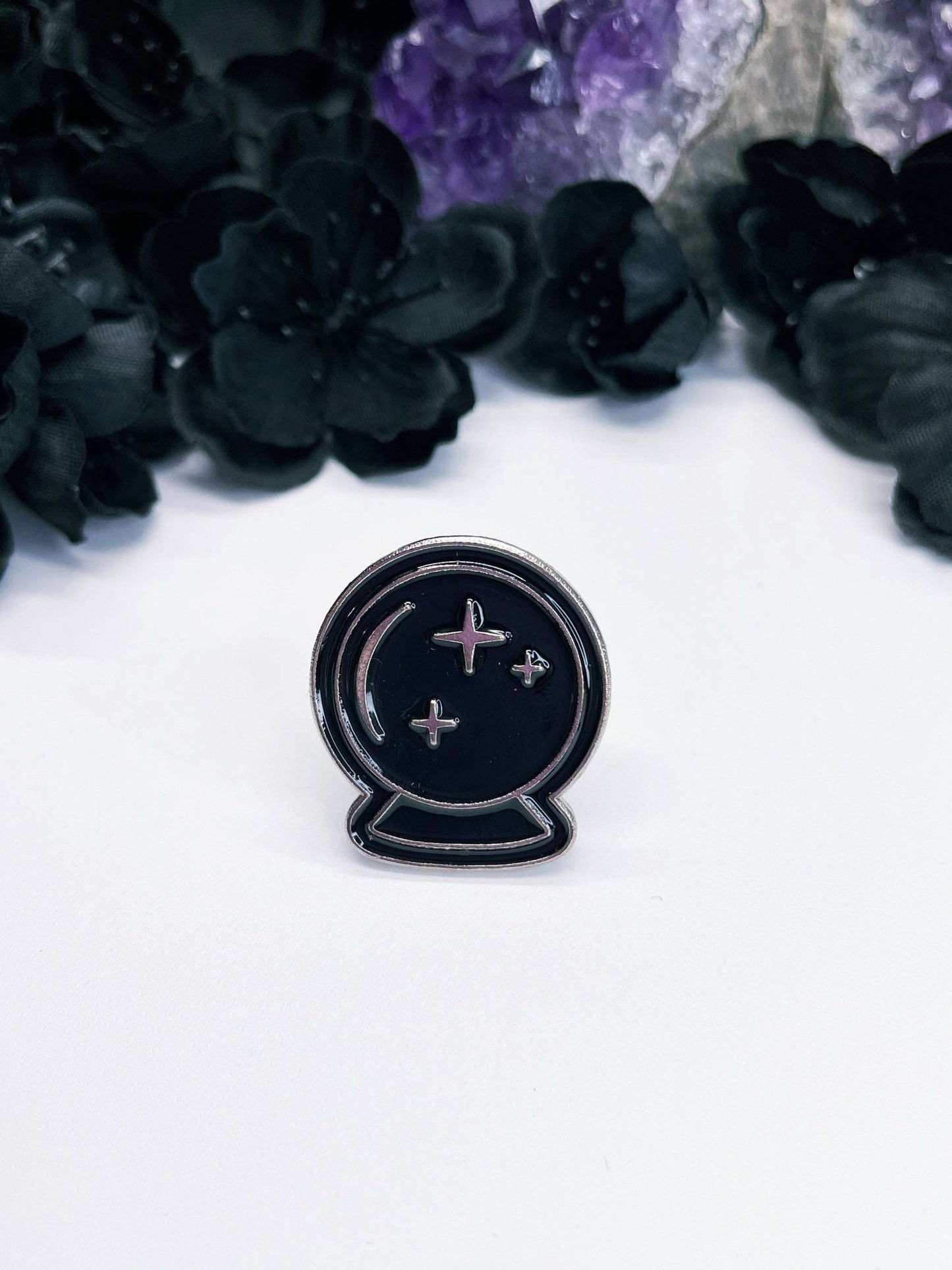 Pictured is an enamel pin of a black crystal ball fortune ball.