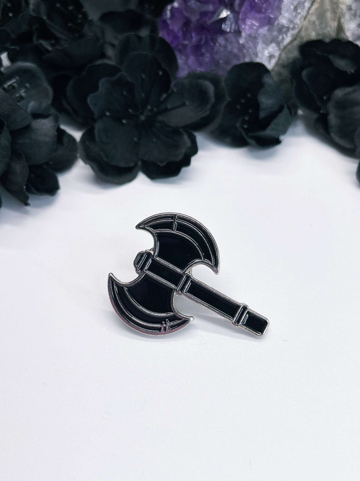Pictured is a black enamel pin shaped like a double-sided axe.